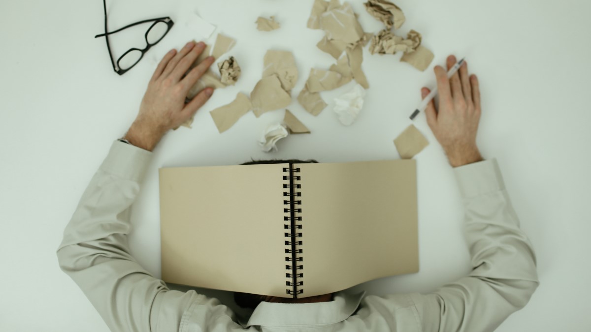 Man met hoofd op bureau met boek over zijn hoofd