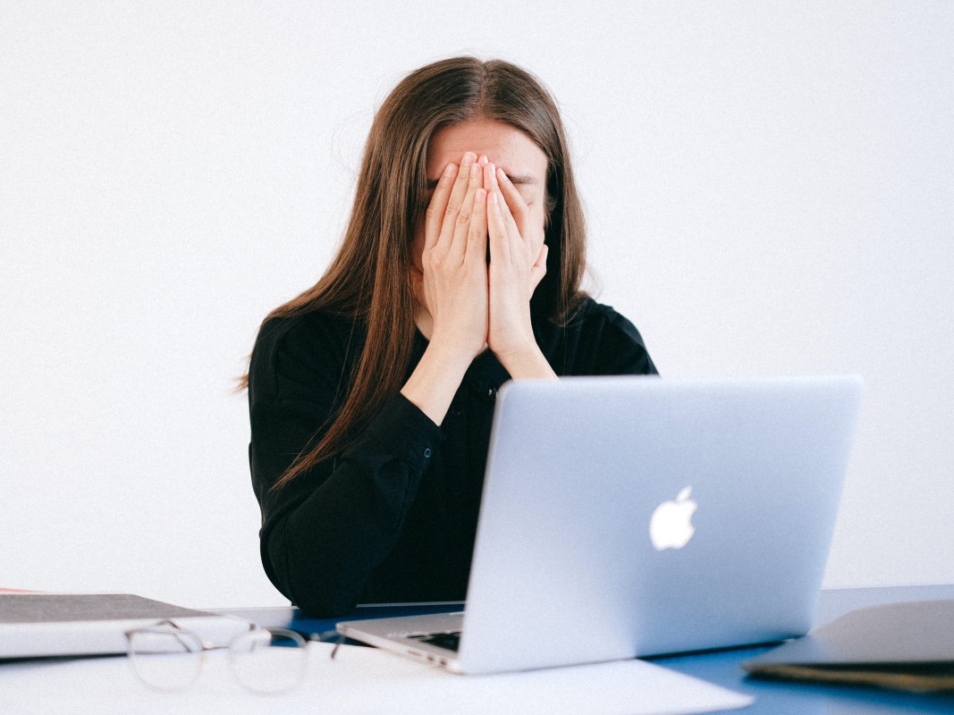 Vrouw achter een laptop met haar handen voor haar gezicht